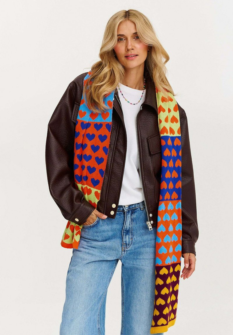 Pletený šál zdobený viaccfarebnými srdcovými vzormi na žiarivom pozadí v oranžovej, modrej a žltej farbe. Materiál pôsobí mäkko a má štruktúru.
