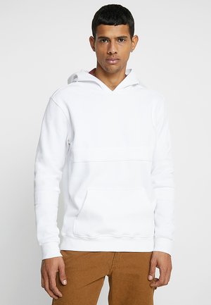 Hvid hoodie med v-hals og frontlomme, med en glat tekstur og lange ærmer. Sammen med brune bukser.