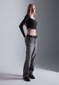 Black ribbed crop top with buttons, high-waisted gray jeans, and black shoes. The jeans feature a relaxed fit and visible stitching.