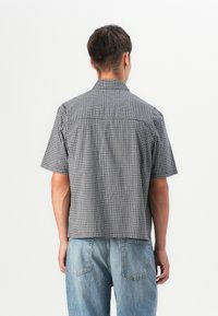 Short-sleeve, collared shirt in black and white check pattern, featuring a straight hem and a relaxed fit, made of lightweight fabric.