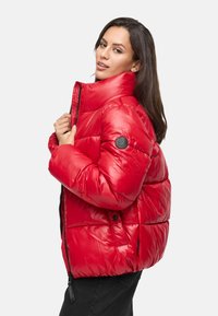 Chaqueta de plumas roja con acabado brillante, alto cuello y parche de logo negro en la manga. Presenta cierre de cremallera y diseño acolchado para aislamiento.