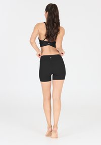 Ensemble de vêtements de sport noir comprenant un soutien-gorge de sport avec un design à croix dans le dos et un short taille haute, fabriqué dans un tissu extensible.