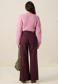 Pull en tricot texturé rose à manches longues, associé à un pantalon large bordeaux. Un sac à imprimé léopard est posé sur un bras.