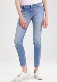 Jasnoniebieskie rurki z denimu z efektem sprania, z pięcioma kieszeniami i zapinane na suwak, zestawione z białymi wsuwanymi trampkami.