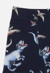 Granatowe legginsy z wzorem dinozaura i pterozaura. Wykonane z miękkiej, rozciągliwej tkaniny z elastycznym pasem i kontrastującymi przeszyciami.