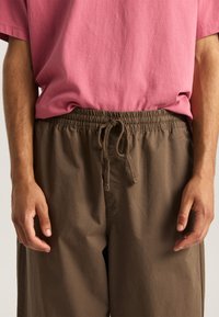Brown, elastic waistband shorts with drawstring detail, paired with a pink cotton t-shirt, featuring a relaxed fit and smooth texture.
