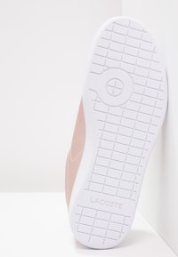 Lacoste sneaker with a smooth light pink upper, white rubber sole featuring a textured grip pattern, and embossed branding on the heel.