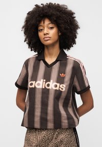 Brown and beige striped short-sleeve polo shirt featuring a black collar, an "adidas" logo in light pink, and three red stripes on the shoulders.