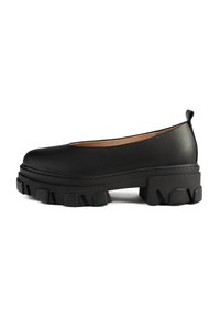 Zapatos de plataforma de cuero negro con punta redonda, que cuentan con una suela de goma gruesa y texturizada y un diseño de corte bajo en la parte posterior.
