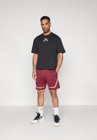 Čierne tričko s krátkymi rukávmi a logom na hrudi, v kombinácii s vínovými športovými šortkami so svetloružovým lemem a čiernymi športovými topánkami.