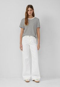 Gestreepte katoenen t-shirt in zwart en wit, gecombineerd met brede witte denim broeken. Sneakers met een beige zool maken de look compleet.