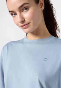 Jasnoniebieski bawełniany sweatshirt z okrągłym dekoltem i małym haftowanym logo na piersi. Miękka tekstura i luźny fason.