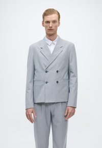 Ανοιχτό γκρι διπλό όρθιο κουστούμι με διακριτό καρό σχέδιο, που διαθέτει σκούρους κουμπιά, δύο μπροστινές τσέπες και κομψή εφαρμογή.