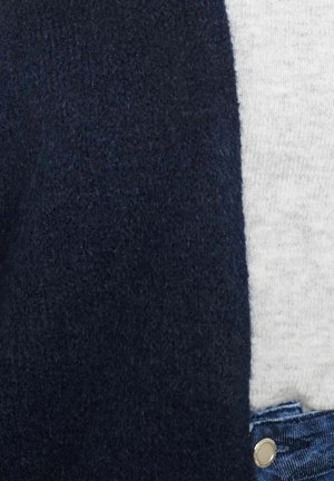 Tumesinine paksu kudumisega kardigan, pehme tekstuuriga, koos heleda halli T-särgi ja teksapükstega, millel on metallnuppude detail.