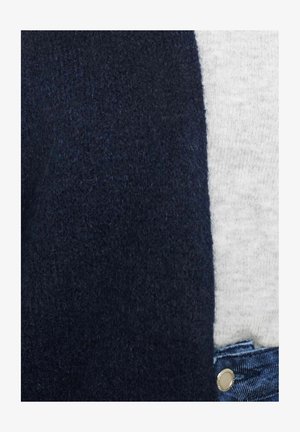 Tumesinine paksu kudumisega kardigan, pehme tekstuuriga, koos heleda halli T-särgi ja teksapükstega, millel on metallnuppude detail.