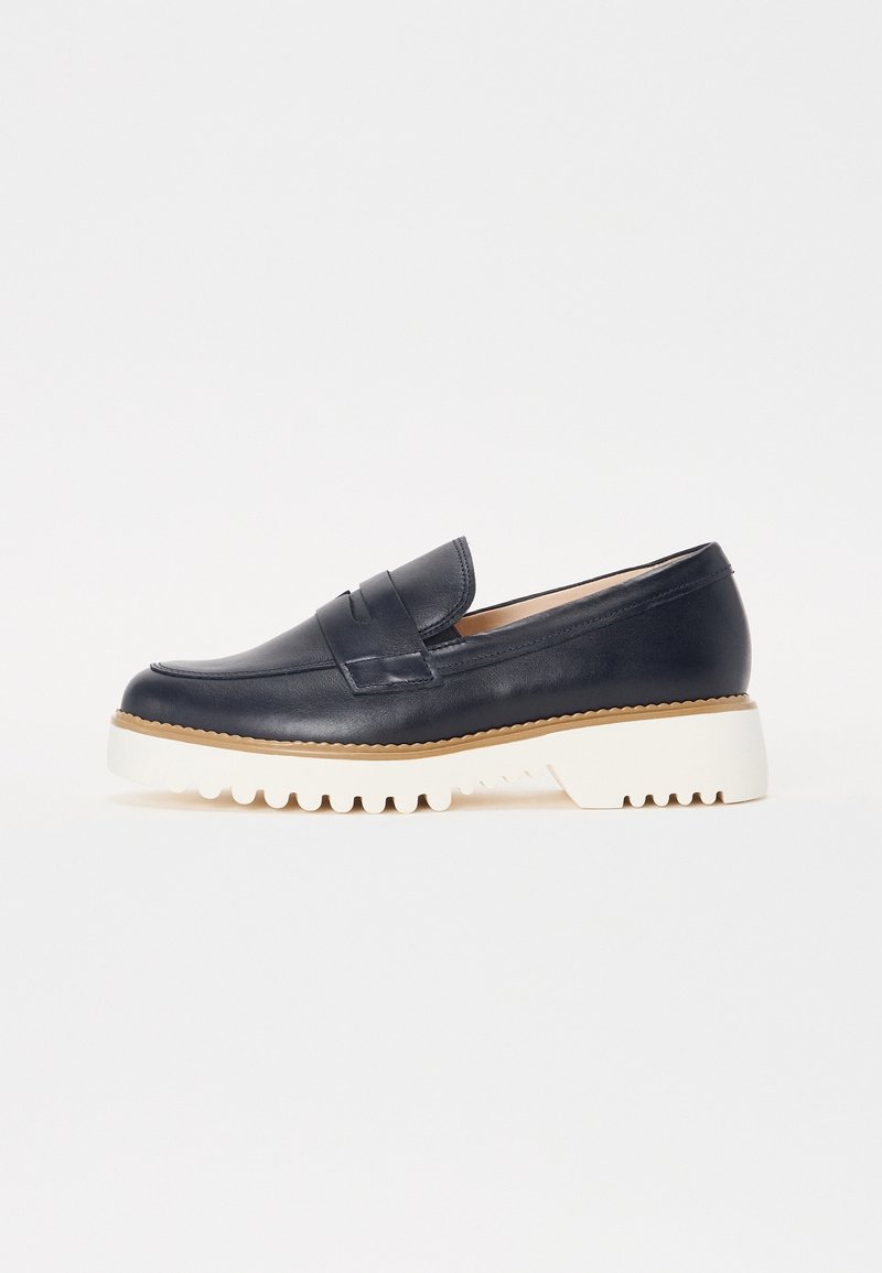 Mocassin en cuir noir avec semelle en caoutchouc blanche épaisse et couture beige sur le pourtour, présenté en profil latéral sur fond blanc.