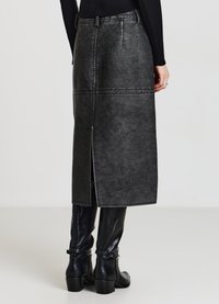 Gonna midi in ecopelle nera con pannelli cuciti e spacco posteriore, abbinata a stivali neri alti fino al ginocchio con dettaglio fibbia.