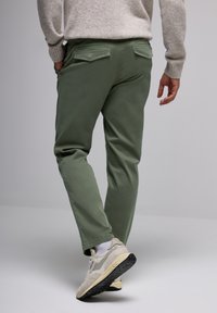 Green cotton pants with back pockets, worn with beige sneakers and white socks, paired with a light gray knitted sweater.