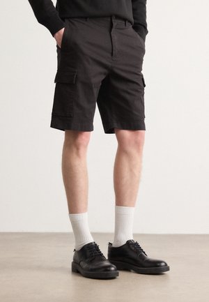 Czarne szorty cargo z bocznymi kieszeniami, wykonane z bawełny. Połączone z czarnymi butami na sznurowadła i białymi skarpetkami do kostek. Prosty, funkcjonalny design.