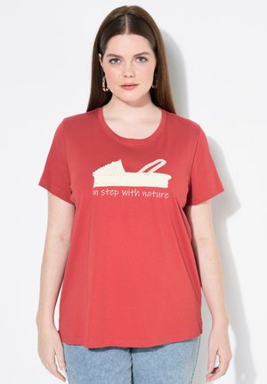 Rotes Baumwoll-T-Shirt mit rundem Ausschnitt, das eine weiße Grafik einer Sandale und den Text "im Einklang mit der Natur" darunter zeigt. Legere Passform.