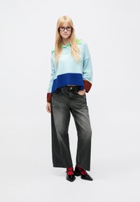 Colorblock knit sweater in light blue, green collar, dark blue band; paired with wide-leg black jeans and red-accented shoes.