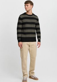 Black and cream striped knit sweater with a crew neckline, worn with beige cargo pants and gray sneakers with white stripes.