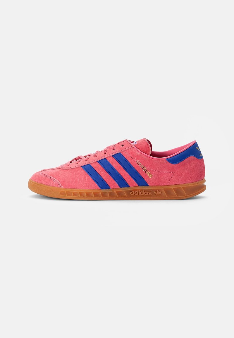 Roze suede sneaker met blauwe strepen, gumrubberen zool en gouden "adidas" branding. Rond neus, platte veters en gevoerde kraag.