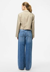 Kort beige jakke med lange ærmer, kombineret med lyseblå viddebenede denimjeans med baglommer og højtaljet.