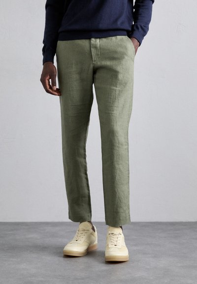Pantalon en lin vert clair avec une coupe droite et des poches latérales, assorti à des baskets jaune pâle. Tissu texturé avec des plis minimes.