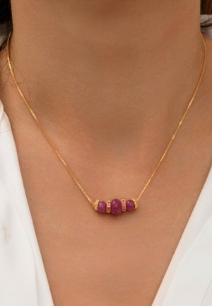 Collier en or ornée de quatre pierres roses, trois de forme ovale avec des accents dorés et une pierre ronde, reposant sur un cou nu.