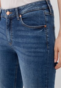 Mörkblå denimjeans med slim fit, featuring kopparfärgade knappdetaljer, ton-i-ton sömmar och traditionell femfickdesign. Slät textur.