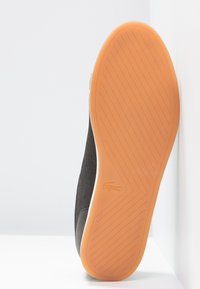Svart sko med orange gummisula, uppställd med sulan riktad framåt, med texturerat grepp och en liten djur logo nära klacken.