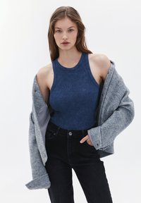 Marinblå, ribbade linne kombinerat med högmidjade svarta denimjeans, lager på lager under en grå oversized ullrock med en mjuk textur.