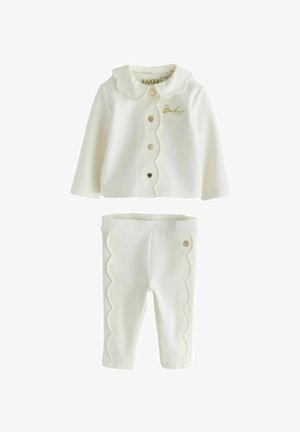 Dvodijelna dječja odjeća u krem boji. Gornji dio ima ovratnik s valovitim rubom i zlatne gumbe; hlače imaju rub s valovitim detaljima i zlatnu oznaku. Mekani materijal.