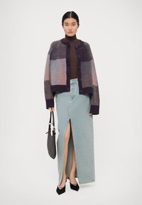 Multi-colored knitted cardigan with a checkered pattern, paired with a brown turtleneck and light blue denim skirt featuring a front slit.