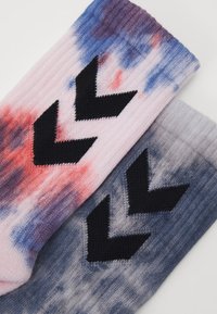 Stickade strumpor med en tie-dye mönster i rosa, blått och grått som har tre svarta chevronränder på varje strumpa. Texturerad ribbad design.