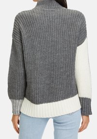 Stickad tröja med hög krage, i grå färgskala med vita ribbade fållar. Texturerad med en lös, grov stickdesign.