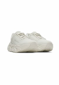 Chunky white sneakers with a textured mesh upper, thick sole, and rounded shape. Features lacing system and subtle branding on the side.