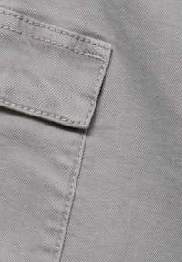 Sivi denim tkanina s vidljivim šavovima. Ima džep na gornjoj lijevoj strani, koji pokazuje glatku teksturu i suptilan sjaj.