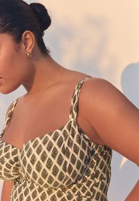 Costume da bagno con motivo a diamante verde e crema, coppe imbottite, spalline larghe e dettaglio in metallo dorato. Tessuto liscio con un design aderente.