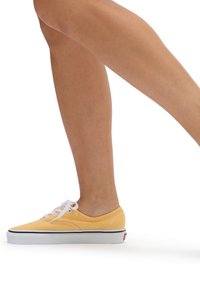 Baskets en toile jaunes avec des lacets blancs, profil bas, semelle en caoutchouc noire et accents de couture blancs. Pied positionné à mi-pas.