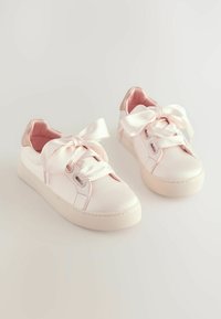 Baskets en satin rose avec de grands noeuds, semelles en caoutchouc texturé et un design épuré. L'intérieur présente une doublure rose douce et un talon renforcé.