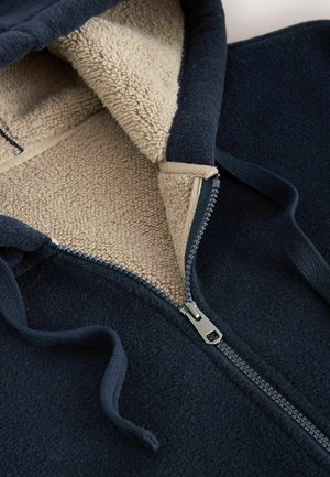 Námořnický fleece zip hoodie s béžovou měkkou podšívkou a šedým zipem, s kapucí na šňůrku a texturovaným vnějším materiálem.