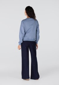 Lichtblauwe sweater met geribde manchetten en zoom, gecombineerd met donkerblauwe wijde jeans met subtiele geborduurde patronen.