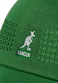 Green Kangol cap made of textured fabric with a kangaroo logo and name embroidered in white. Features patterned sections on sides.