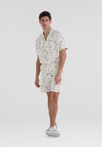 Beige Kurzarmhemd und Shorts-Set mit abstrakten schwarzen Mustern, aus leichtem Stoff, kombiniert mit weißen Sneakers.
