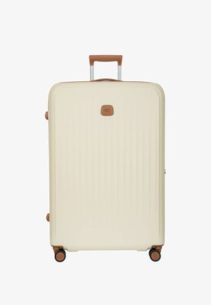 Valigia rigida color crema con manico e ruote marroni, in piedi con manico telescopico esteso.