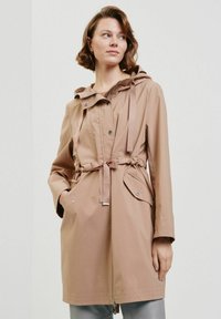 Beżowa wodoodporna kurtka z kapturem, sznurkiem w talii i przednimi kieszeniami. Posiada zamek błyskawiczny i zatrzaski, gładką teksturę oraz lekki materiał.