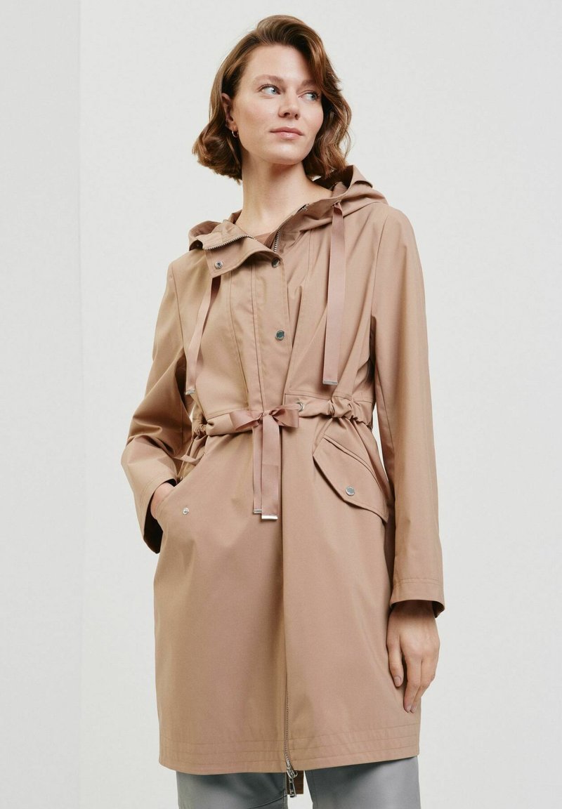Beżowa wodoodporna kurtka z kapturem, sznurkiem w talii i przednimi kieszeniami. Posiada zamek błyskawiczny i zatrzaski, gładką teksturę oraz lekki materiał.