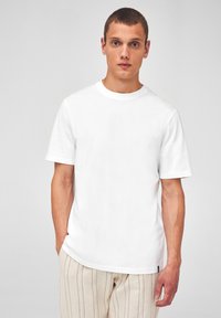 T-shirt en coton blanc avec un col rond et des manches courtes, présentant une coupe droite et un design minimaliste.